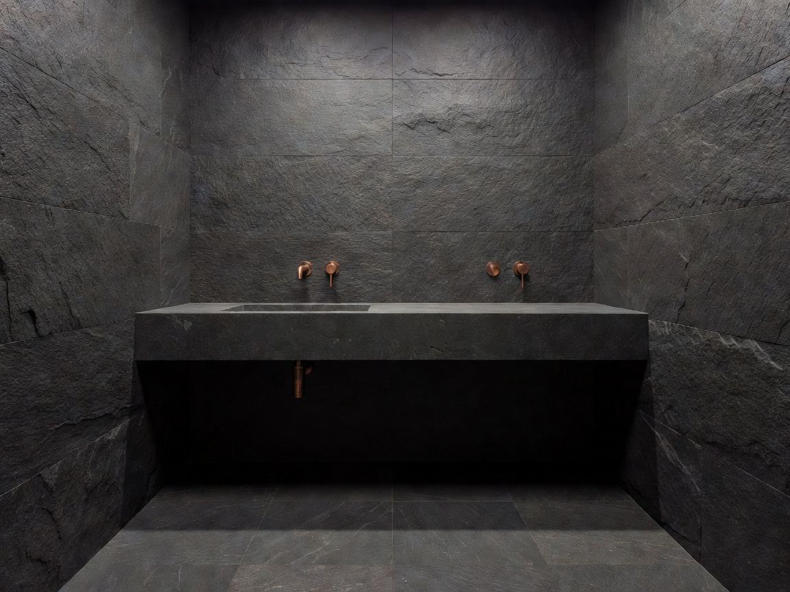 Minimalist moody bathroom clad in grey and black textured basalt tiles and custom copper faucets
